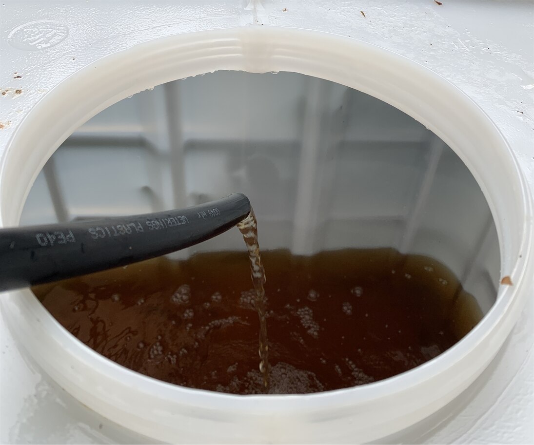 braunes Wasser fließt aus Schlauch in weißen Container